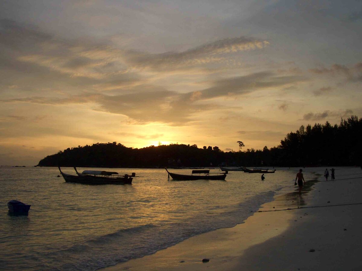 Pattaya Beach at dawn: longtail boats in silhouette and people walking along the water