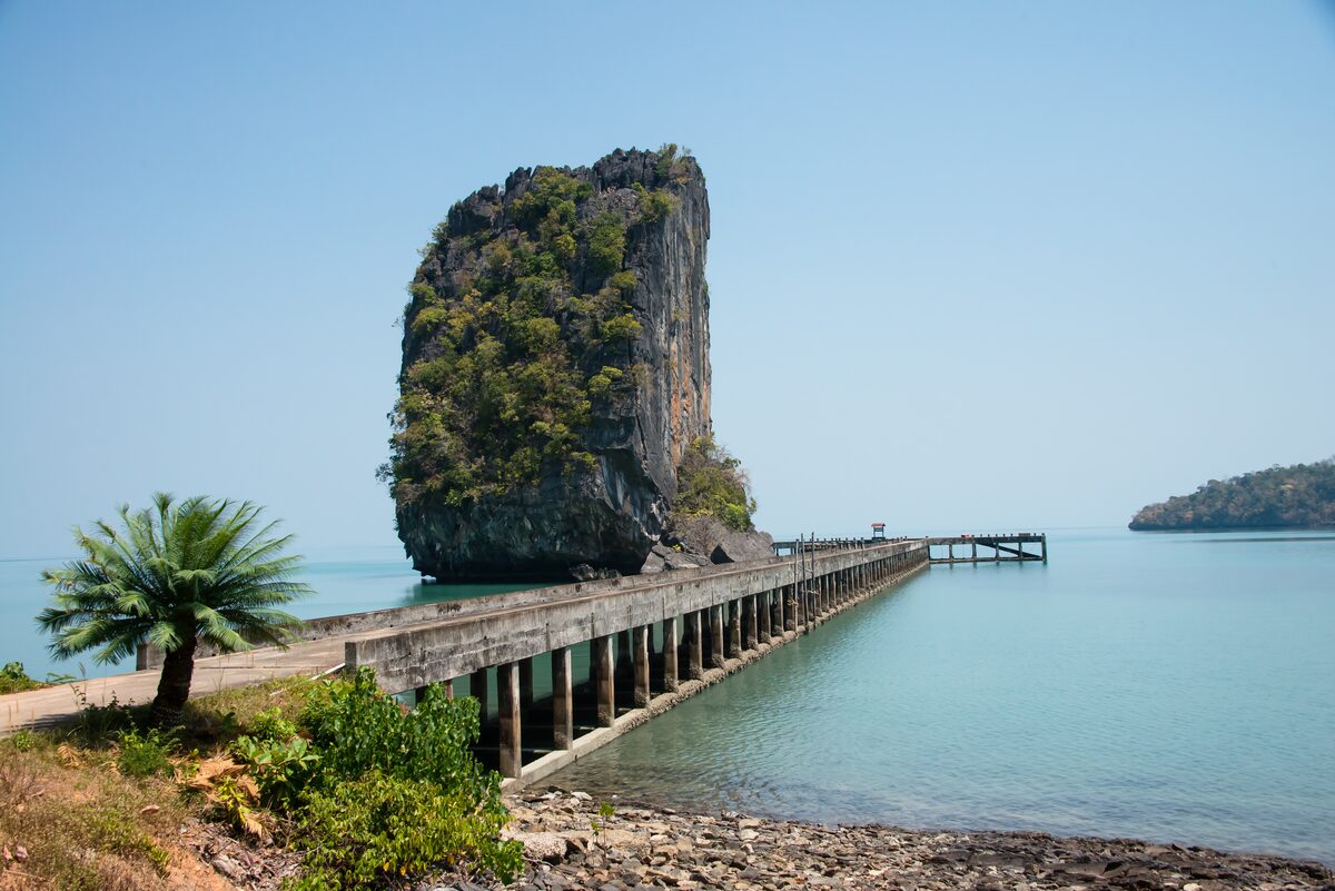A long concrete pier leading past a tall limestone rock into turquoise water